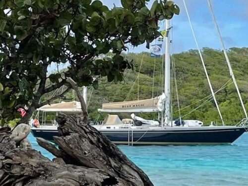 Sailboat named Blue Magic anchored near a rocky shoreline with turquoise water and green mangroves in a tropical setting